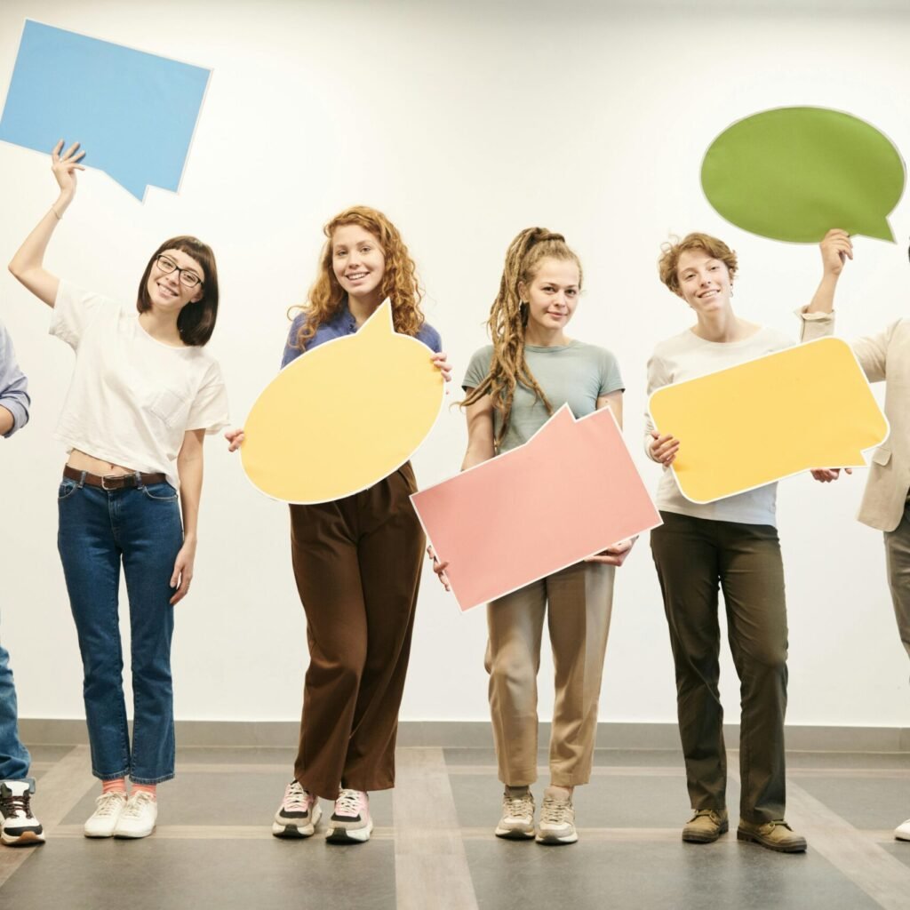 Diverse group of smiling adults holding vibrant speech bubbles indoors.